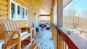 Una cabaña de madera con un porche, una silla, una mesa y vistas al bosque circundante.