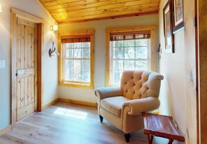 A room with wooden flooring, a tufted armchair, two windows with blinds, and a wooden door. - Switchback Lodge • Pool Table, Dart Board (Sugar Mountain)
