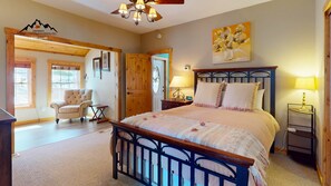 A bedroom with a bed, a chair, a wooden door, a painting, and a lamp. - Switchback Lodge • Pool Table, Dart Board (Sugar Mountain)