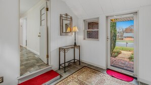 En gang med trappe, et konsolbord med lampe, et spejl og en dør der fører ud.