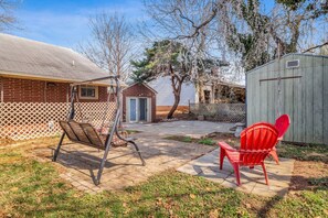 Ein Garten mit Schaukel, einem roten Adirondack-Sessel, einem Schuppen und einem Haus mit umzäuntem Garten.