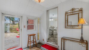 En gang med dør til en terrasse, et klædestativ, et spejl, en lampe og et lille bord.