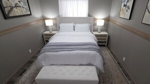 Een hotelkamer met een bed, nachtkastjes, een bankje en kunst aan de muren.