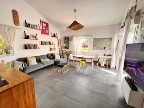 A modern living room with a grey sofa, bookshelves, a wooden coffee table, a TV, and a dining area. - House 5 minutes from the beach (Pérols)