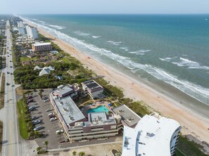 An aerial view of a coastal hotel with a swimming pool, parking, and beachfront access. - Bent Palm 401 (Ormond Beach)
