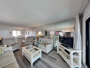 Una sala de estar con sofá, sillones, una mesa de centro, televisor y un espejo grande.
