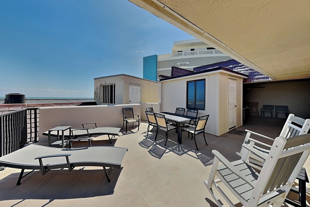 A rooftop terrace with outdoor furniture, a table, and a view of the ocean.