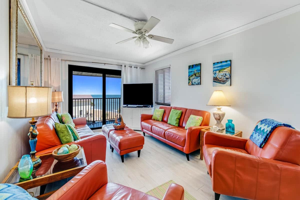 A living room with a balcony, leather sofas, a flat-screen TV, and artwork on the walls.
