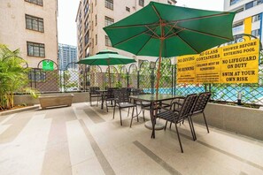 Uma área externa com mesas, cadeiras, piscina e uma placa com avisos de segurança.