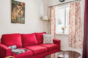 A red sofa, a round coffee table, a wall clock, a window with floral curtains, and a painting of an owl.