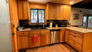 A kitchen with wooden cabinets, a stainless steel dishwasher, a window with a view of trees, and a countertop with a coffee maker. - Cozy 2-bedroom cabin in Pollock Pines, Apple Hill/Gold Country (Pollock Pines)