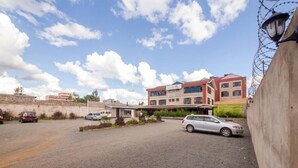 A building with a flat roof and multiple windows, a parking area with several cars, and a clear sky with clouds. - maple Inn Hotel (Ruiru)