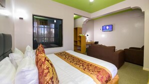 A hotel room with a bed, a television, a desk, and a seating area. - maple Inn Hotel (Ruiru)