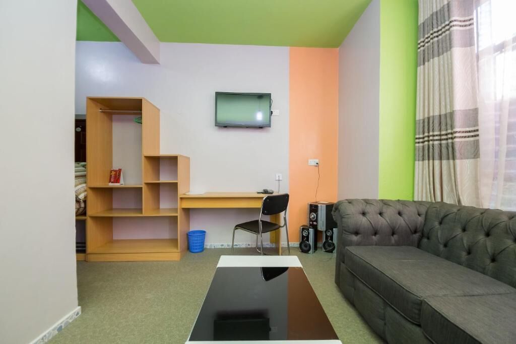 A room with a sofa, a TV mounted on the wall, a desk, and a bookshelf.