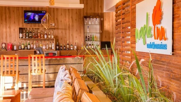 A bar area with wooden decor, a TV screen, and a sign for 'Maple Leaf Annual Conference'. - maple Inn Hotel (Ruiru)