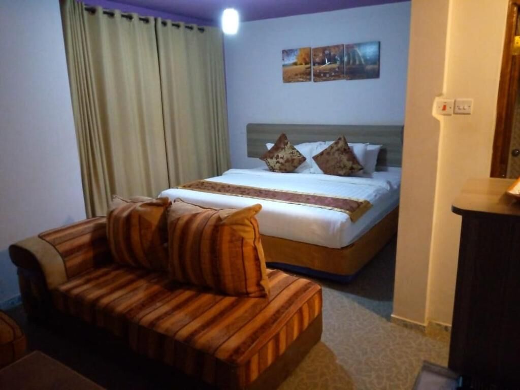 A hotel room with a bed, a wooden sofa, a desk, and a curtain.