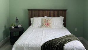 Een slaapkamer met een bed, nachtkastje, lamp, klok en een wandlamp.