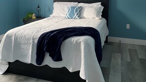 Een slaapkamer met een bed, een donker hoofdbord, een witte sprei en een blauwe muur.