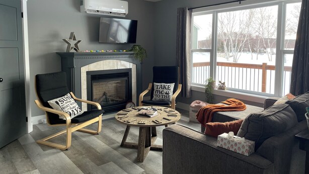 Een woonkamer met een open haard, een televisie erboven en een groot raam met uitzicht op een besneeuwd terras.