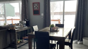 A dining area with a table, chairs, a kitchen counter, and a large window with curtains. - Delightful 2-bedroom cottage with AC. Highway 1 Trans Canada near Badger (Badger)