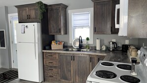 Een moderne keuken met houten kastjes, een witte koelkast, een spoelbak, een fornuis en een raam met jaloezieën.