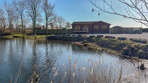 Een vakantiehuis aan het meer, met een houten hutje, een omheind stuk grond en een heldere lucht.