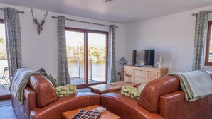 Een woonkamer met een bruine leren bank, een houten salontafel en een televisie op een houten dressoir.
