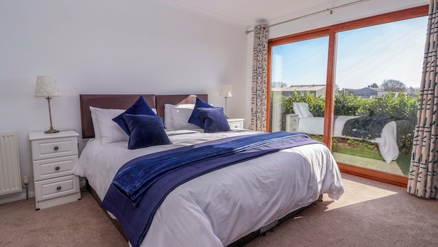 Slaapkamer met een groot bed, nachtkastje, lamp en uitzicht op een tuin door een schuifdeur.