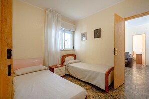 A room with two beds, a window with curtains, a bedside table, and a door leading to another room. - Apartment 'Villa Burdi' with Sea View, Private Terrace and Air Conditioning (Capitolo)