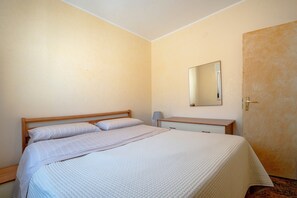 Une chambre à coucher comprenant un lit, une table de chevet, une commode, un meuble à tiroirs, un miroir et une porte.