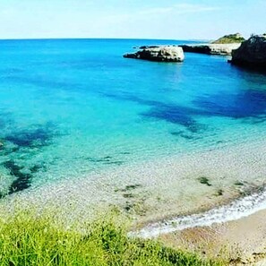 Paesaggio costiero con acqua blu cristallina, formazioni rocciose e vegetazione verde.