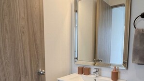 A bathroom with a wooden door, a white sink with a mirror above it, and a towel rack on the wall. - Modern & Exclusive | Stunning View (Manizales)