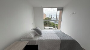 A bedroom with a bed, a small table, and a window with a city view. - Modern & Exclusive | Stunning View (Manizales)