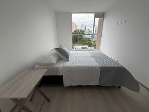 Un dormitori amb un llit, una taula petita i una finestra que dona a una vista de la ciutat.