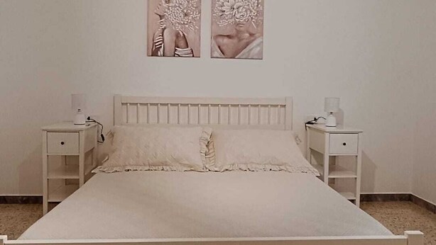 A bedroom with a bed, two nightstands, a wall-mounted light fixture, and two wall art pieces. - Chanzerhouse (Fondi)
