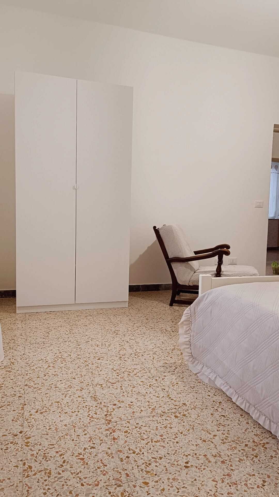 Ein Schlafzimmer mit Bett, Stuhl, Kleiderschrank und einem kleinen Tisch.