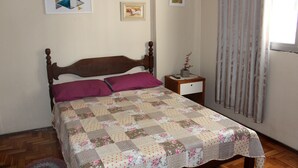 Quarto com cama de madeira, colcha, mesa de cabeceira e janela com cortinas.