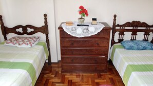 Quarto com duas camas, penteadeira de madeira, toalha de renda e um vaso com flores.