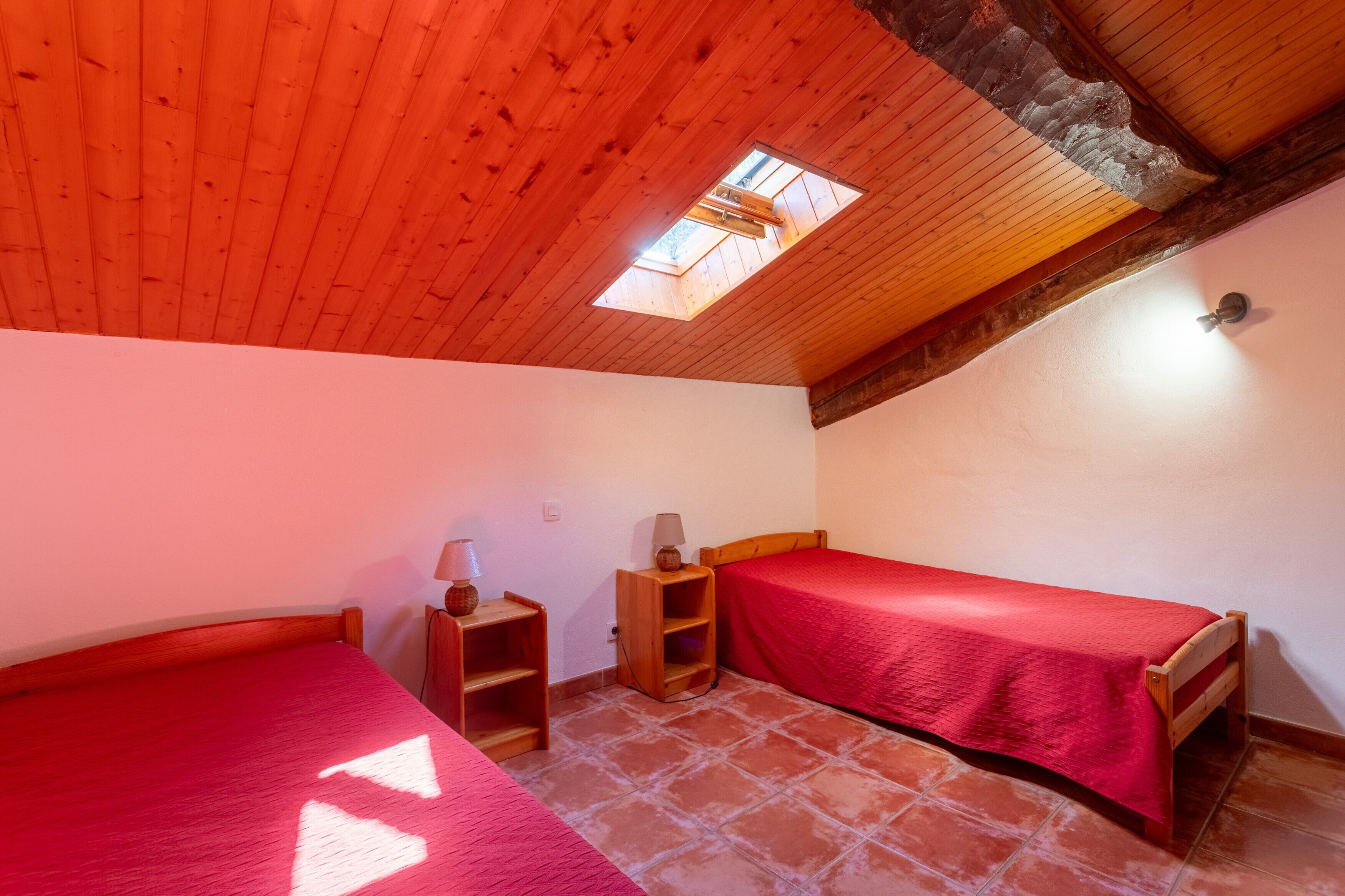 Una habitación con dos camas, un tragaluz, vigas de madera y suelo de baldosas.