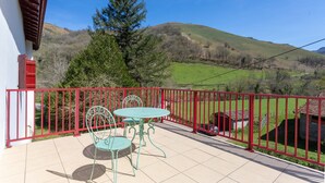 A balcony with a red railing, a turquoise table and chairs, and a view of green hills. - Charming Little Yaitua with Mountain View, Private Terrace and Wi-Fi (Estérençuby)