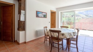 A dining area with a table and chairs, a wooden beam, a picture on the wall, and a view through a glass door. - Charming Little Yaitua with Mountain View, Private Terrace and Wi-Fi (Estérençuby)