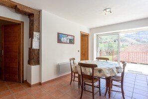 Een eetgedeelte met een tafel en stoelen, een houten balk, een schilderij aan de muur en uitzicht door een glazen deur.