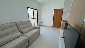 Un soggiorno moderno con un divano, una TV, un tavolino con una pianta e una porta.