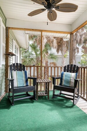 A covered porch with two rocking chairs, a ceiling fan, and a small table. - Pet-Friendly Cottage by the Beach (Folly Beach)
