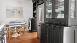 Een moderne keuken met donkere kastjes, een eethoek met tafel en stoelen, en een groot schilderij aan de muur.