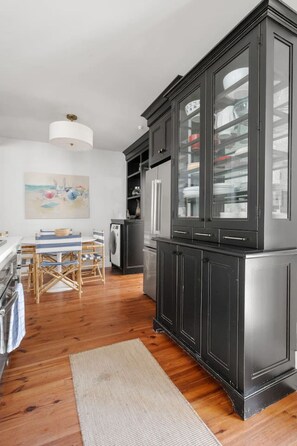 A modern kitchen with dark cabinetry, a dining area with a table and chairs, and a large painting on the wall. - Spring St 2 Bedroom - 3 Blocks to King Street (Charleston)