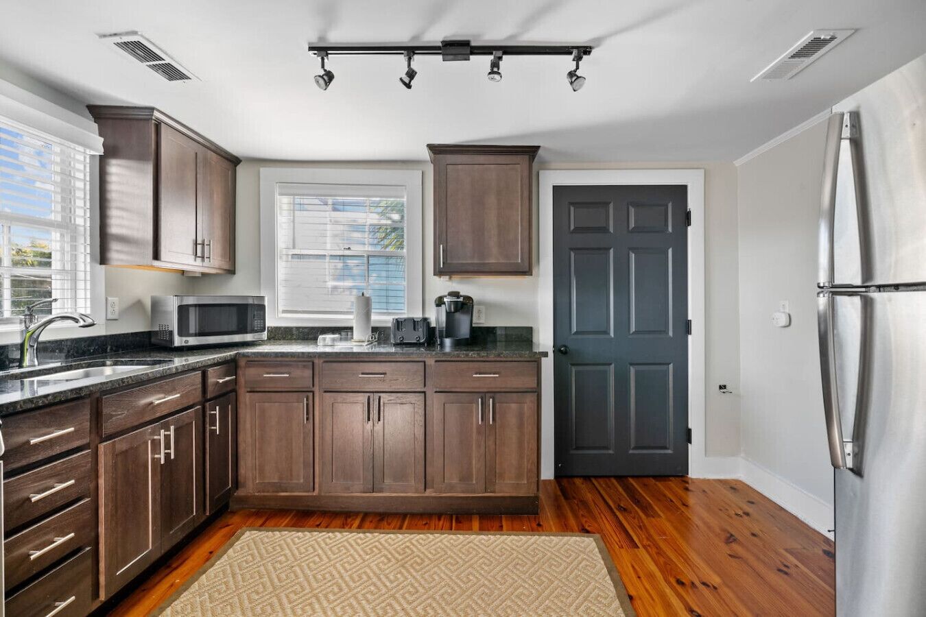 A kitchen with dark wooden cabinets, a stainless steel refrigerator, a microwave, and a coffee maker.