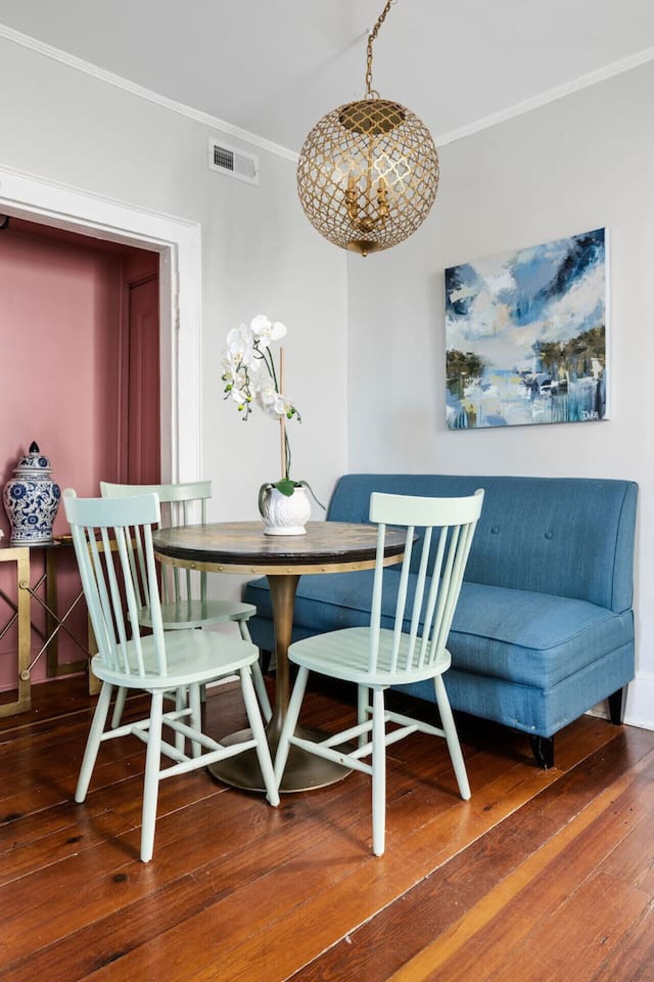 Un comedor con una mesa redonda, dos sillas, un sofá azul, una lámpara colgante y un cuadro en la pared.