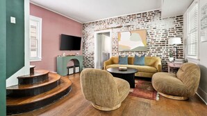 Una sala de estar con pared de ladrillo, un sofá, dos sillones, una mesa de centro y un televisor de pantalla plana.