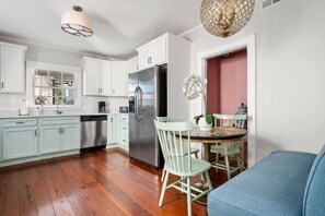 A modern kitchen with white cabinets, a stainless steel refrigerator, and a dining area with a round table and chairs. - Chic Spring St Retreat / Walk to King St-3 Blocks (Charleston)